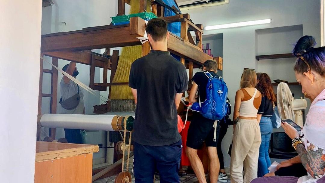 visitors observing the loom, with the weaver and developing fabric clearly visible